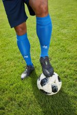 A pair of blue team socks worn by a player, standing on a soccer ball on green grass.
