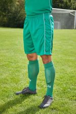 Green sports shorts with light green side stripes, worn with matching long socks, set against a grassy field.