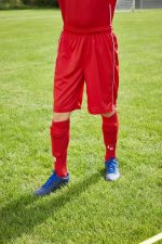 Red sports shorts with an elastic waistband, paired with blue shoes and red socks, situated on grass.