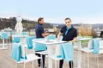 A fleece blanket in a soft blue hue drapes over white outdoor dining chairs on a balcony.