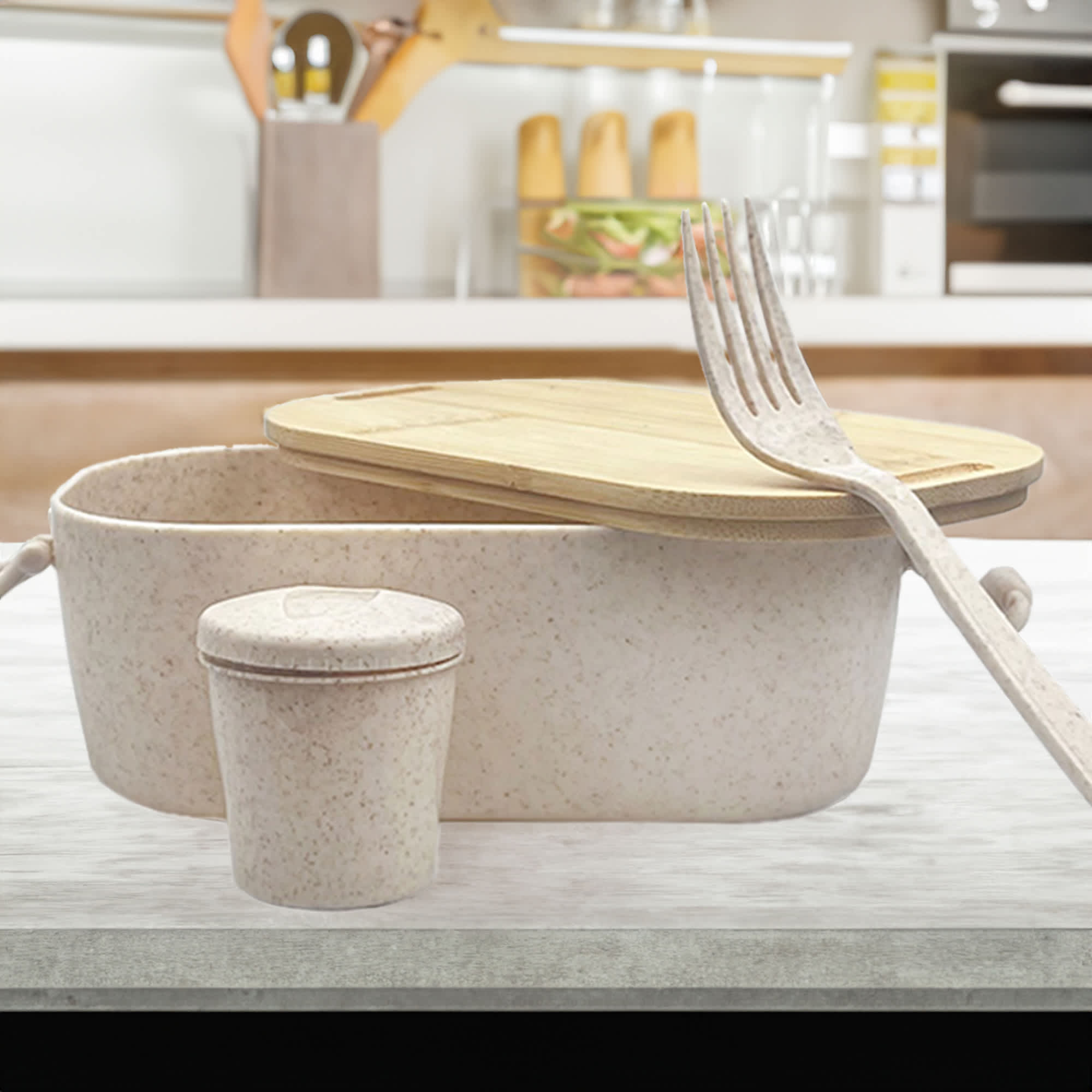A bamboo lunch box with a light pink hue, accompanied by a small container and a fork, set on a kitchen countertop. Handy Man Bamboo Lunch Box - Image 1