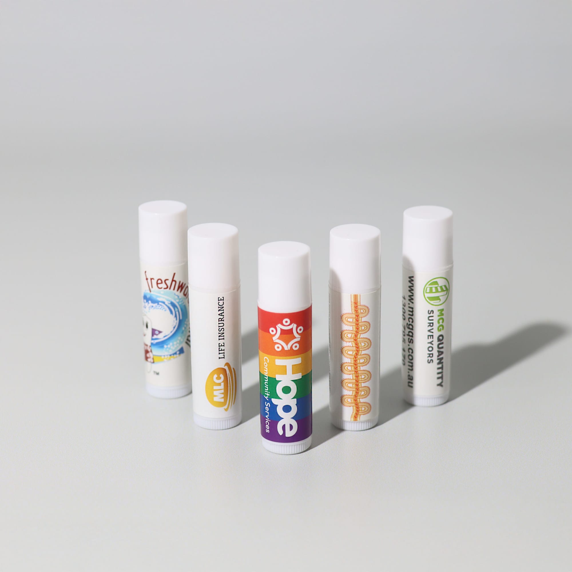 A selection of five lip balm tubes in various designs and colours, all featuring white caps and different labels. Lip Balm - Image 1
