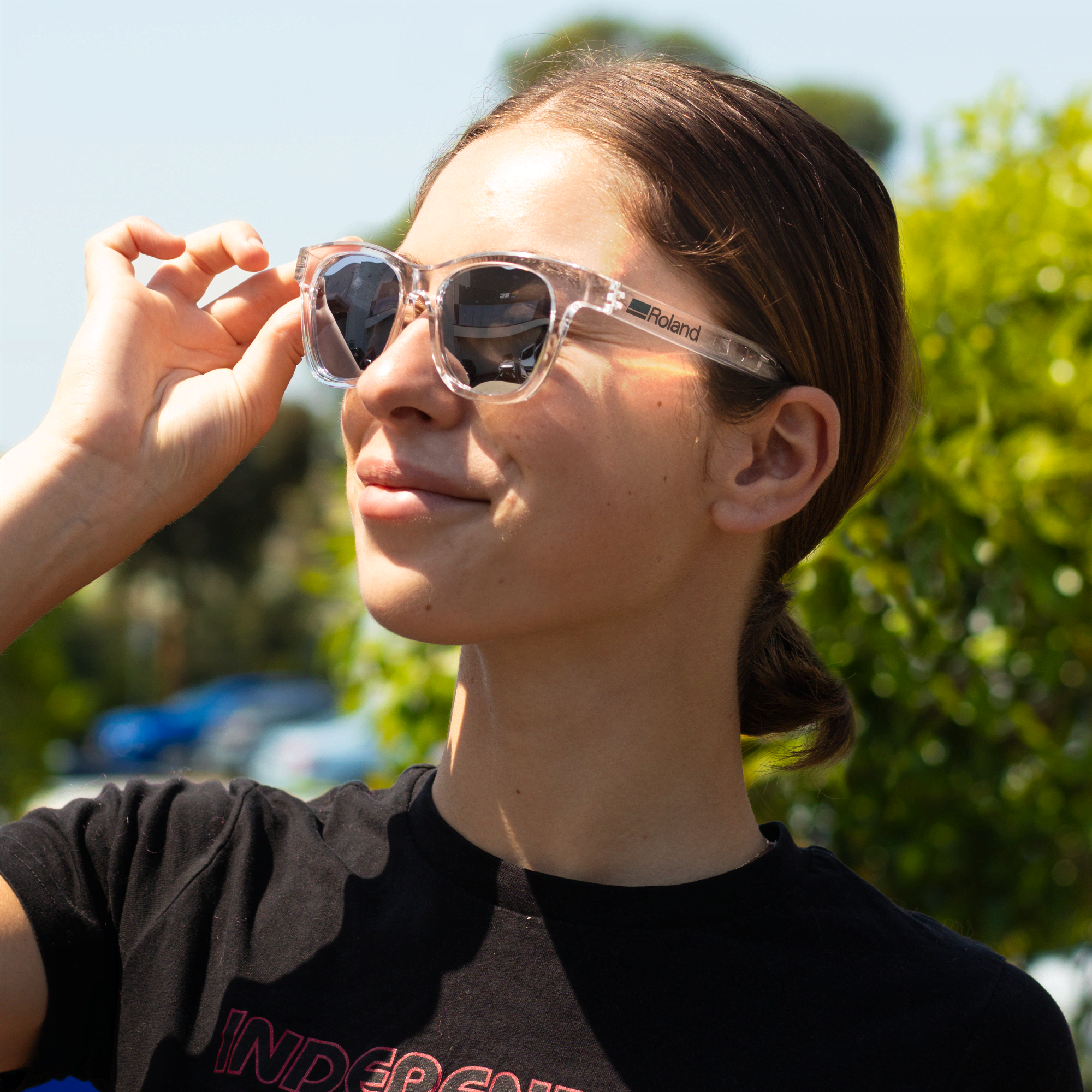 A pair of clear and dark grey polarised sunglasses worn by a person with a ponytail, outdoors. Summer Polarised Sunglasses - Image 1