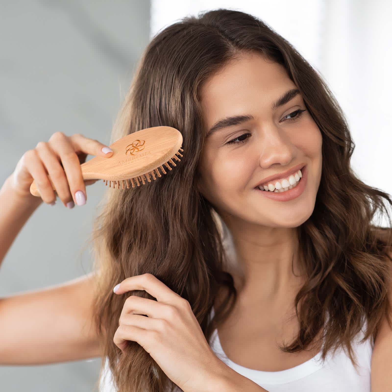A bamboo hair brush with wooden bristles, held by a woman with wavy, dark hair, smiling in a bright setting. Spa Bamboo Hair Brush - Image 1