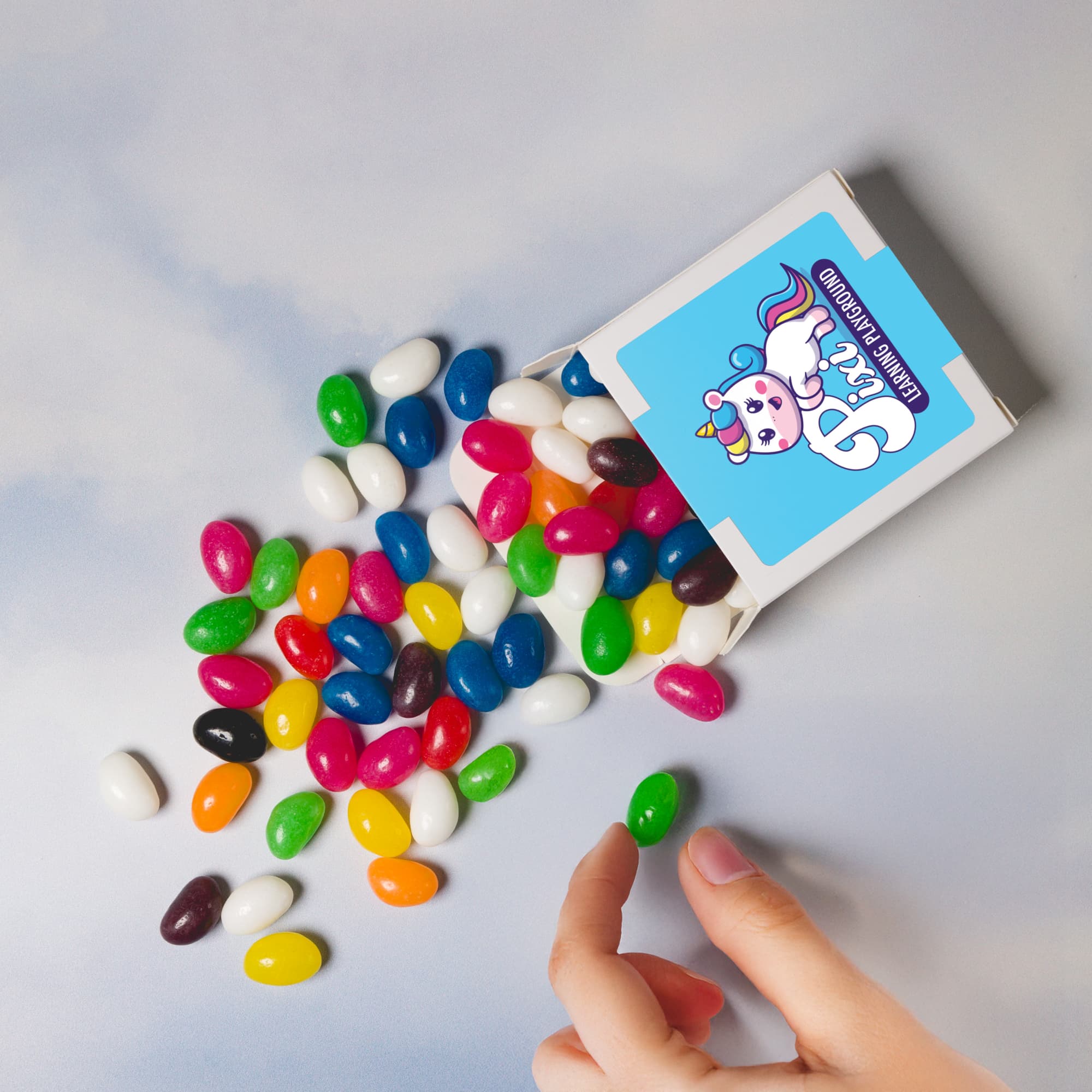 Assorted colorful jelly beans in various shades spilling from a 50g box. The box has a logo design. Assorted Colour Jelly Beans in 50g Box - Image 1