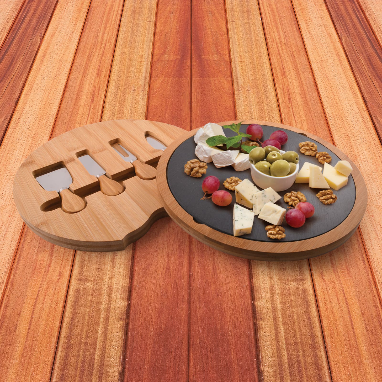 A bamboo cheese board with a slate surface, featuring assorted cheeses, olives, grapes, and walnuts. It includes knife slots. Gala Bamboo Slate Cheese Board - Image 1