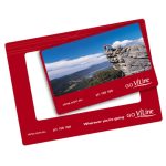 A red magnetic photo frame featuring a scenic landscape image and a logo. It has a slot for a photo.