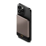 A slim, magnetic wireless power bank in grey is attached to the back of a black smartphone. It features a logo.