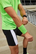 A green sporty wristband worn on the wrist of a person in a bright green shirt and black shorts.