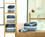 A selection of grey and white guest towels neatly folded on a wooden shelf and a countertop, with a towel set beside a bathtub.
