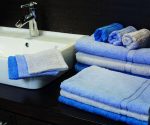 A collection of blue and light blue towels neatly arranged on a counter beside a sink.