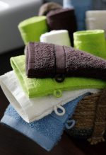 A collection of towels in various colours, including green, white, brown, and blue, neatly arranged in a basket.