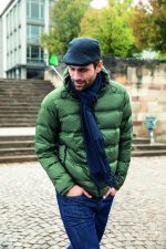 A man in a green puffer jacket and dark scarf walks on cobblestone steps. The scarf has a subtle fringe detail.