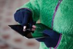 Touch-screen fleece gloves in navy, being used to interact with a tablet, paired with a green fleece jacket.