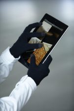 Black touch-screen knitted gloves are used to operate a tablet device, showcasing a sleek design.