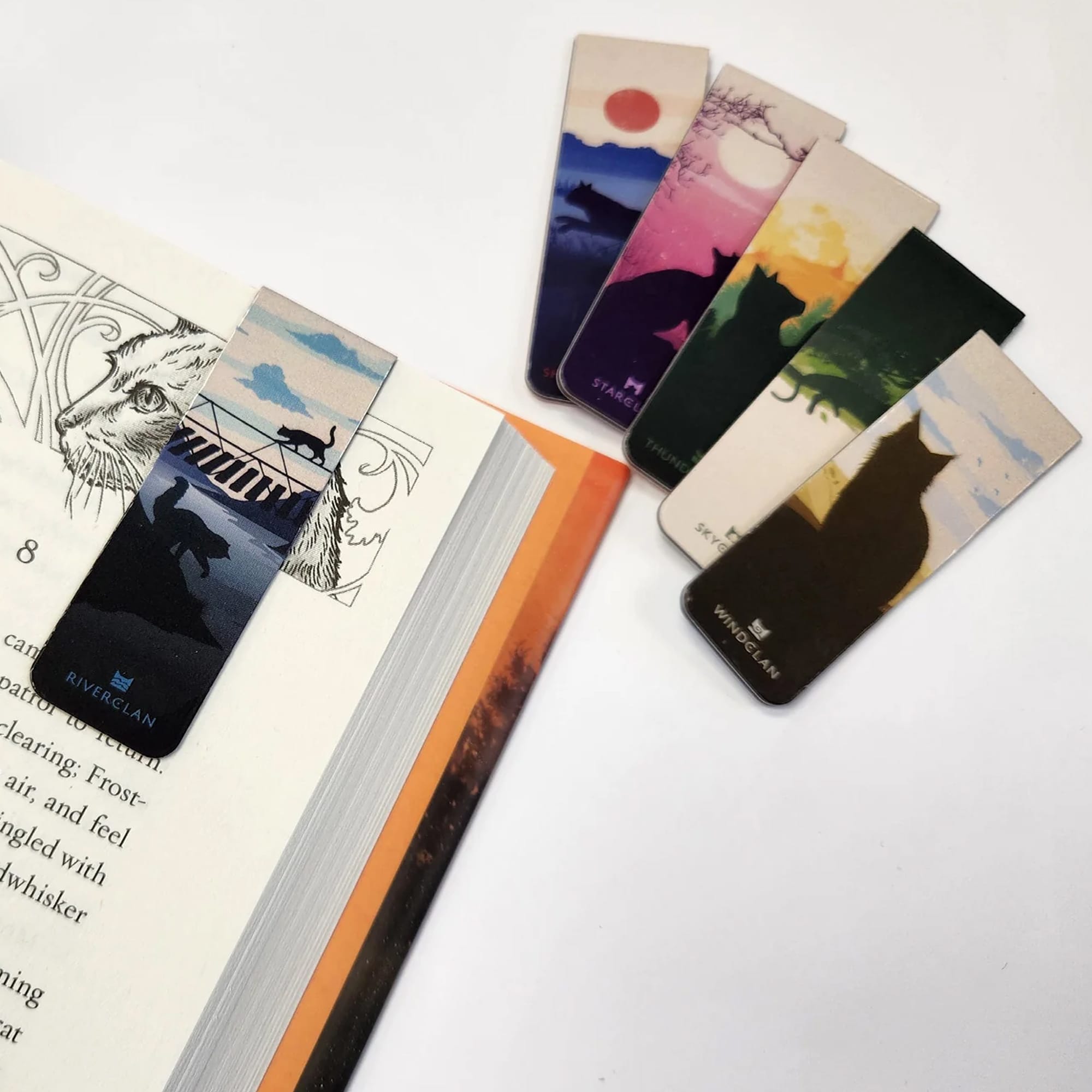 A set of colourful bookmarks featuring various designs and a fridge magnet resting on an open book. Fridge Magnet and Book Mark – Small - Image 1