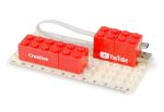 A red USB flash drive designed like Lego blocks, connected to a ruler with a base plate. It features logos and creative text.