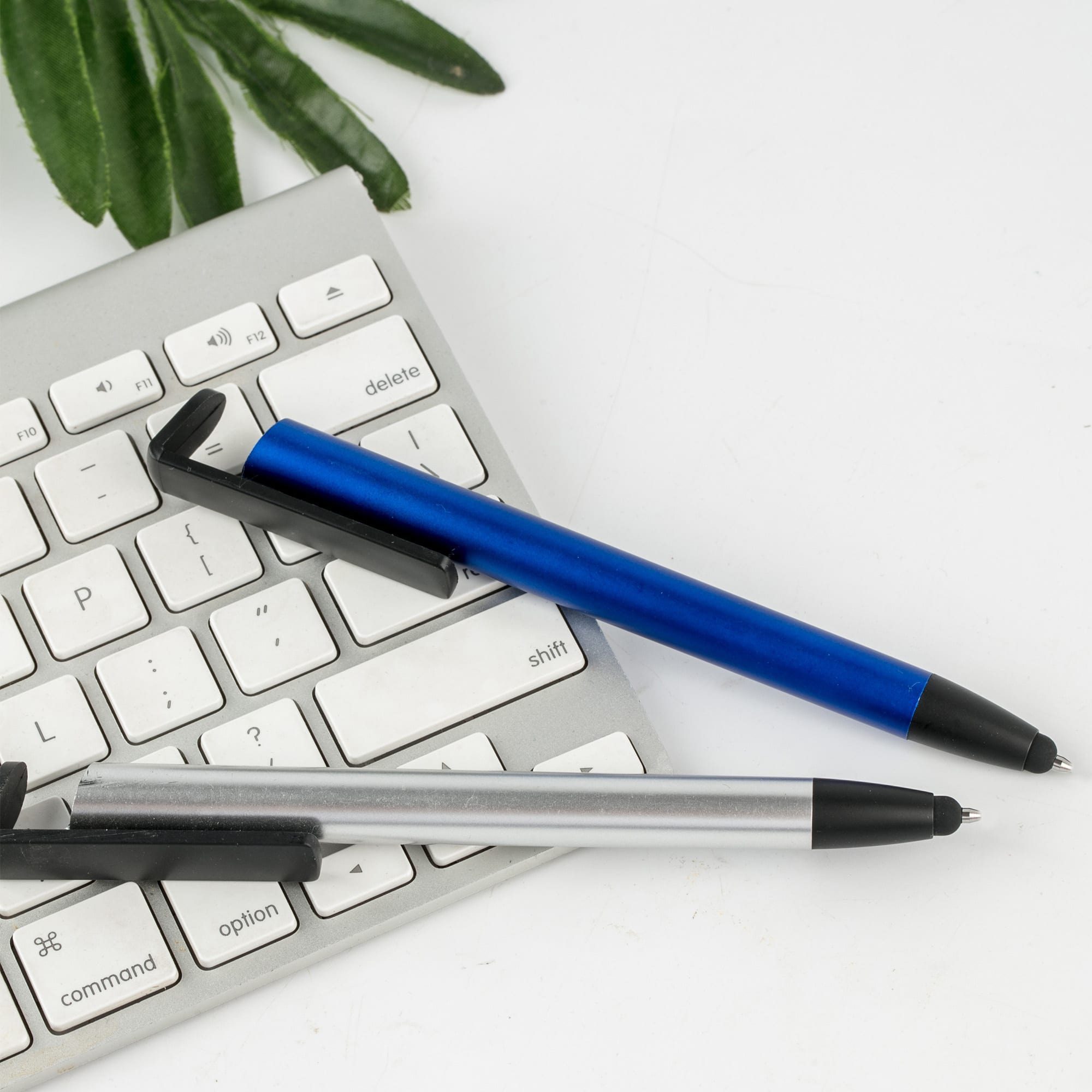 A blue and a silver plastic pen rest beside a computer keyboard on a white surface. Stylus I-Stand Plastic - Image 1