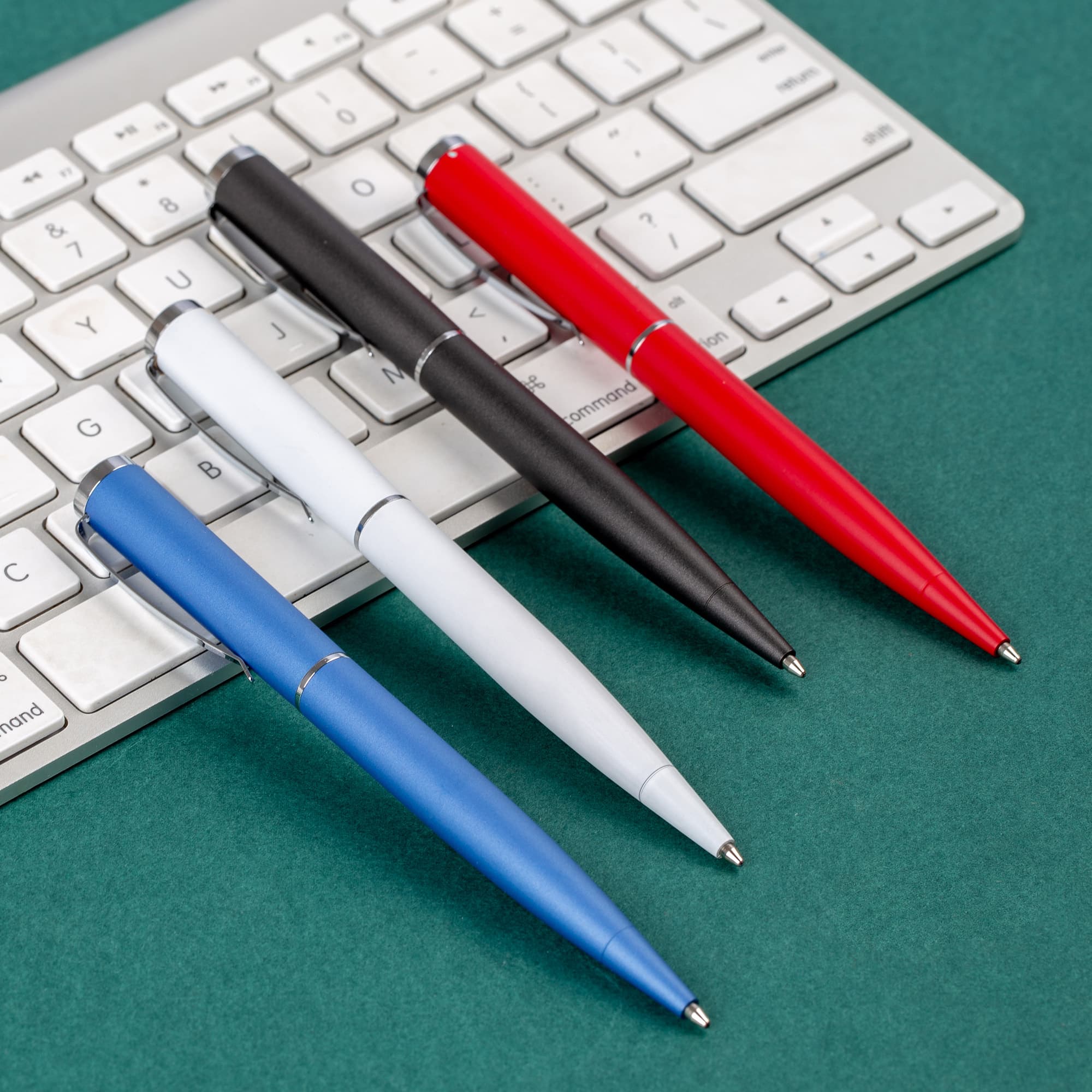Metal pens in blue, white, black, and red placed on a grey keyboard against a green background. World Prestige - Image 1