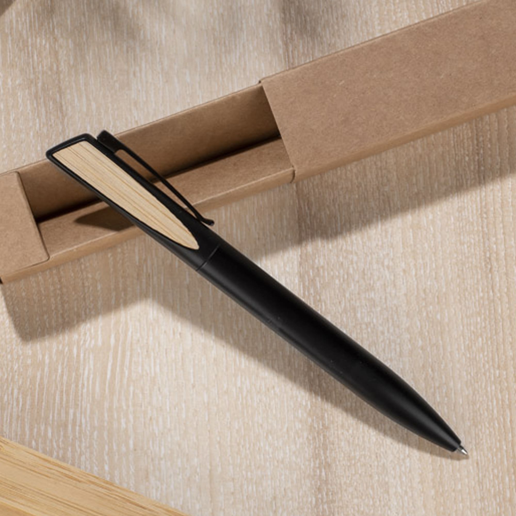 A black metal pen with a wooden accent, resting on a light wooden surface near a cardboard box. Lanzer - Image 1