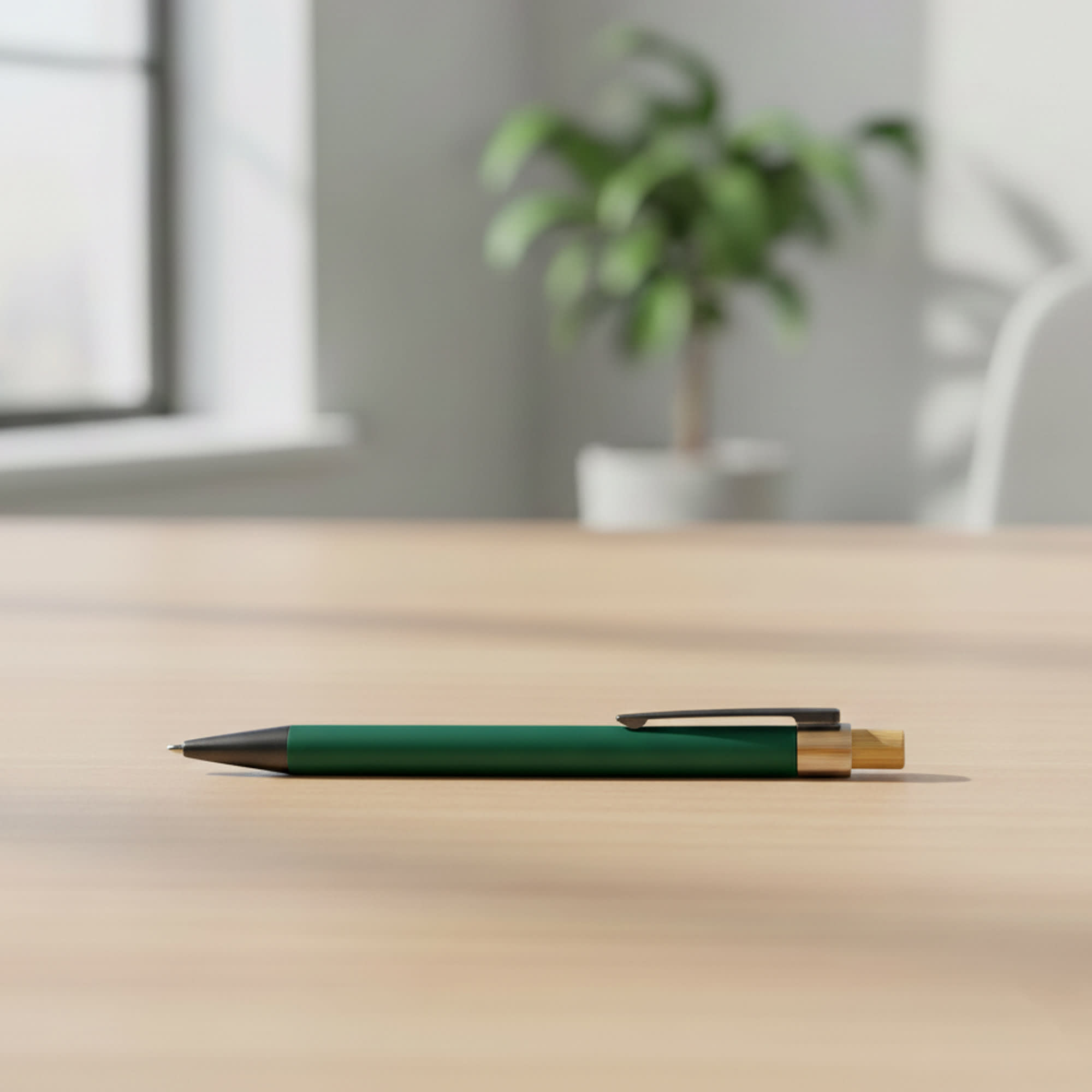A green metal pen with a gold clip rests on a wooden table, with a plant in the background. Sio Metal Pen - Image 1