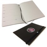 A dark notebook with a logo, featuring lined pages and an elastic closure, shown open and closed.
