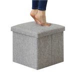 A grey foldable storage ottoman with a textured fabric, featuring a person’s bare feet on top.