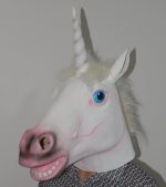 A unicorn mask in white with a pink snout, blue eyes, and a horn, worn by a person against a plain background.
