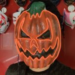 A pumpkin-shaped mask with an angry expression, featuring bright orange and green colours, illuminated with LED lights.