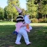 A person wearing a large white unicorn inflatable costume with a pink hat and a striped sweater.