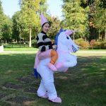 A woman in a white and pink unicorn inflatable costume with a pointed hat, set in a grassy park.