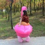 A pink inflatable flamingo costume worn by a person, set in a grassy, tree-lined outdoor area.
