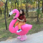 A pink flamingo inflatable costume designed for fun, featuring a person seated inside. Trees and a path in the background.