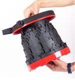 A red and black telescopic stool with a handle, held by a person, showcasing its collapsible design.