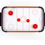 An air hockey table game in red and white, featuring pucks and goalies on a dotted playing surface.