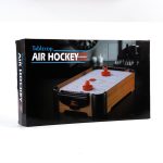 A tabletop air hockey game in a box, featuring a wooden design and red pucks. The packaging has a logo.