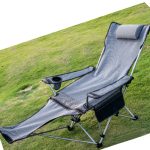 A grey camping lounge chair with a headrest and side pocket on a grassy surface. It has a frame for support.