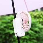 A rechargeable folding hand-held fan in white, featuring a clip attachment for support, set against a green backdrop.