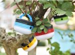 Portable camping lights in blue, red, yellow, and green hanging from a tree amidst green leaves.