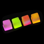 Four brightly coloured light-up ice cubes in pink, green, and orange, emitting a glowing effect against a dark background.