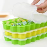A silicone ice cube tray with lids in green and yellow, filled with various frozen fruits.