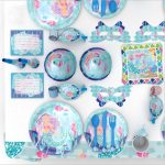 A set of customised disposable party tableware in shades of blue, featuring mermaid designs, includes plates, cups, and utensils.