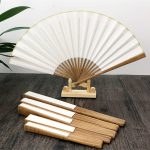 A folding fan with a wood frame and white fabric, displayed on a stand, alongside several matching wooden handles.