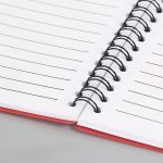 A red spiral notebook with lined pages, featuring black metal spirals and a smooth finish.