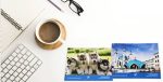 A set of microfiber glasses cloths featuring images of puppies and a building, with a white mug and keyboard in the background.