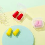 Earplugs in various colours—red, pink, and yellow—packaged in a clear case on a pastel background.