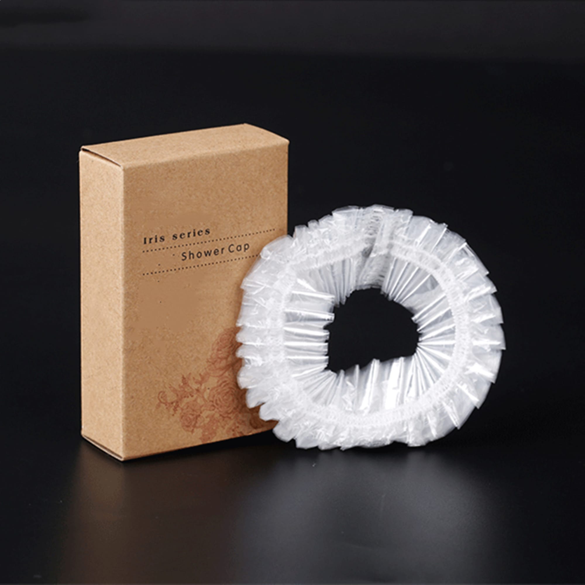 A clear disposable shower cap packaged in a brown cardboard box, featuring a logo. A clear disposable shower cap packaged in a brown cardboard box, featuring a logo.