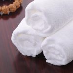 White rolled bath towels stacked on a wooden surface, beside a decorative bead bracelet.