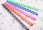 A set of colourful, segmented magic rulers in green, pink, blue, orange, and black, arranged in a line on a patterned surface.