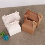 Two Gable Boxes in white and brown, featuring handles and positioned on a textured surface, with decorative coloured balls nearby.